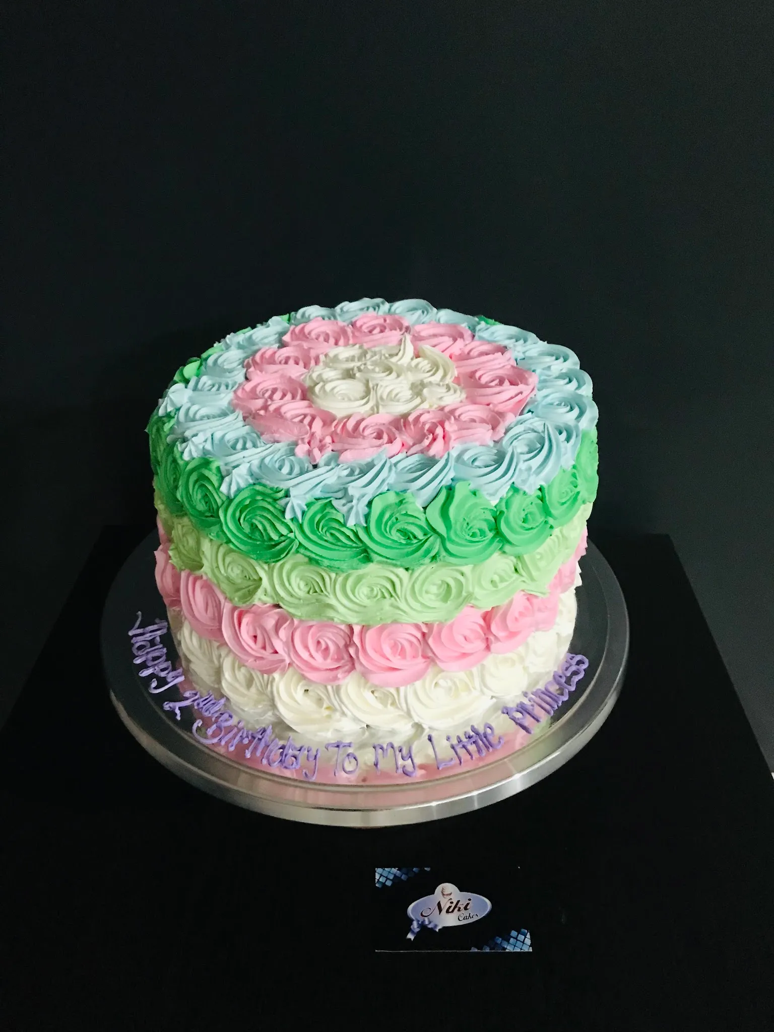 Round birthday cake with pastel multicolour buttercream rosette piping in pink, blue, green and white bands