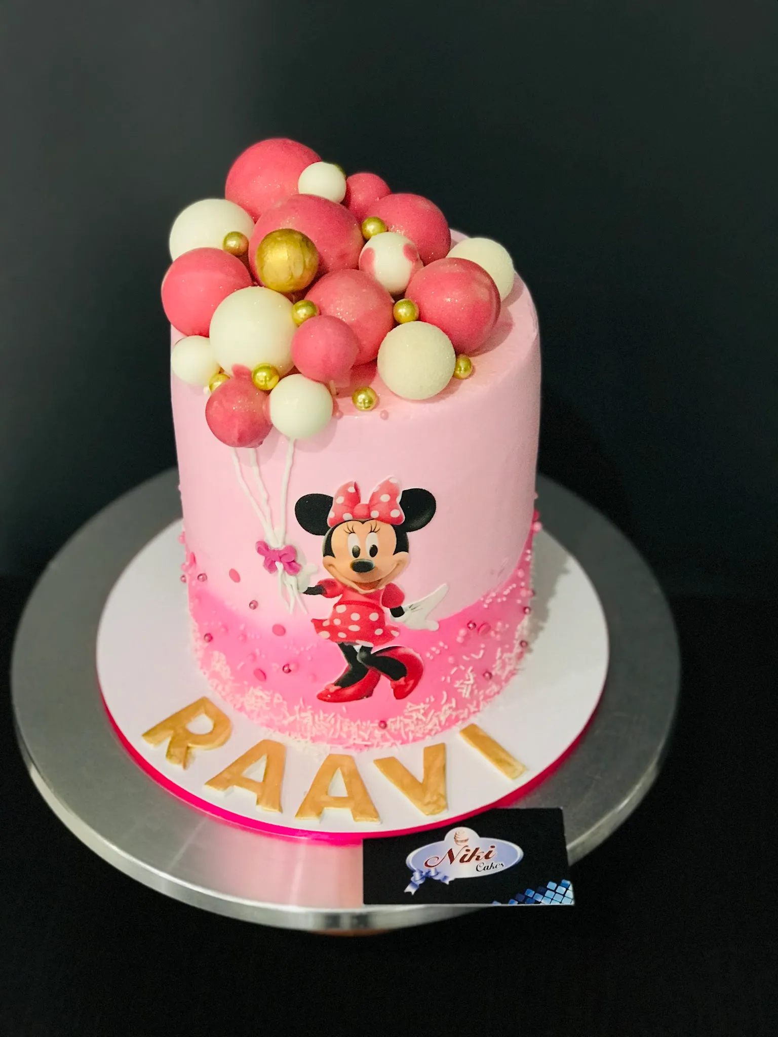 Pink Minnie Mouse birthday cake with chocolate sphere balloon topper and gold letter name tiles