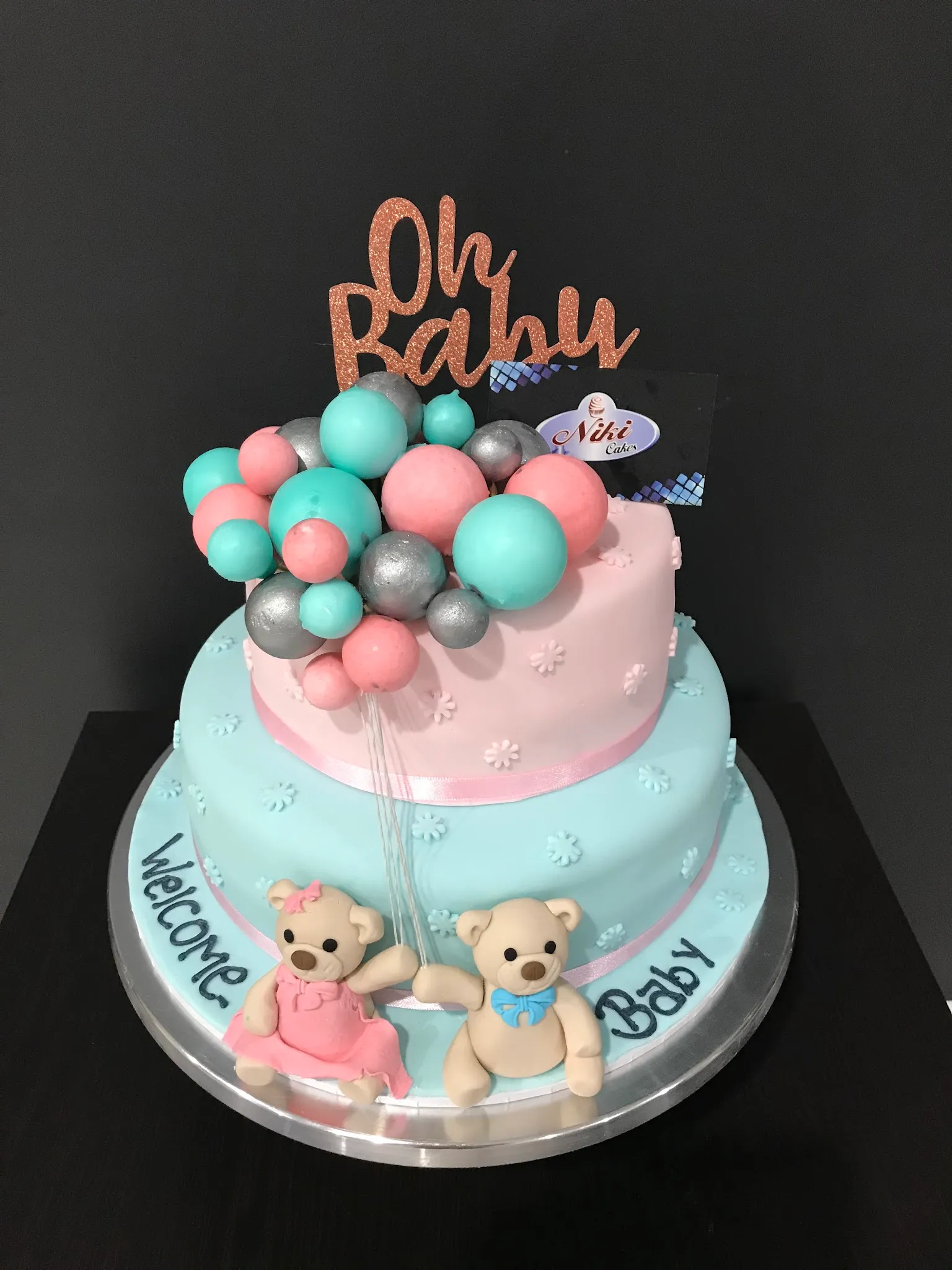 Two-tier baby shower cake in pale blue and pink with teddy bears, balloon sphere garland and Oh Baby topper