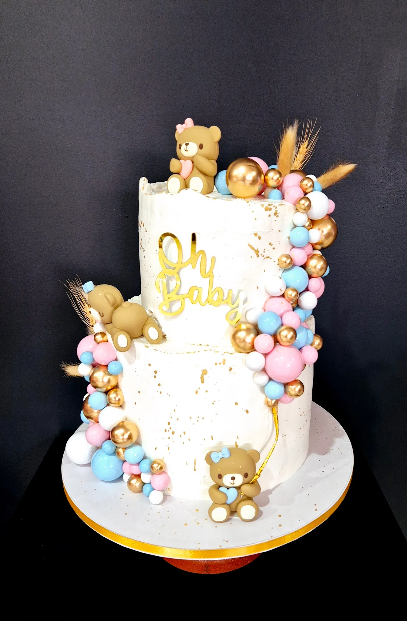 Two-tier white textured baby shower cake with sugar roses, gold pearls and Krishna figurine decorations